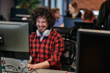 Afro saç stili ve ekose gömlekli bir programcı, modern ofis ortamındaki bir bilgisayarda özenle kodluyor.
