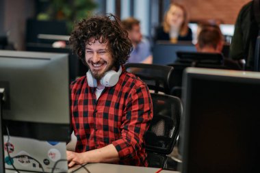 Afro saç stili ve ekose gömlekli bir programcı, modern ofis ortamındaki bir bilgisayarda özenle kodluyor.