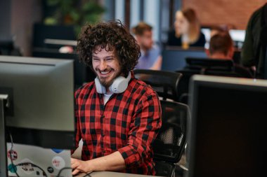 Afro saç stili ve ekose gömlekli bir programcı, modern ofis ortamındaki bir bilgisayarda özenle kodluyor.