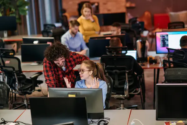 stock image Business colleagues, a man and a woman, engage in discussing business strategies while attentively gazing at a computer monitor, epitomizing collaboration and innovation. 