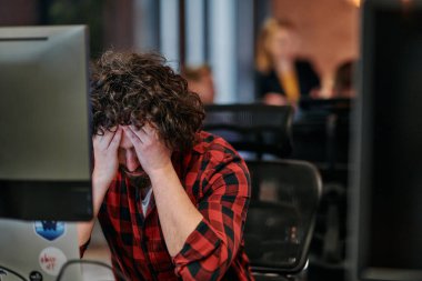 Dağınık saçlı bir programcı oturur, bilgisayar monitörüne hayal kırıklığı dolu bir bakışla bakar, teknik zorlukları yansıtır..