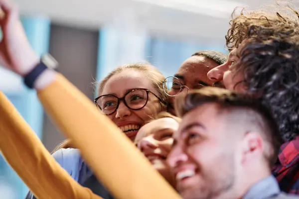 stock image A diverse group of business professionals take a break from their tasks in a modern startup office to capture a creative selfie, showcasing teamwork and a vibrant workplace culture. 