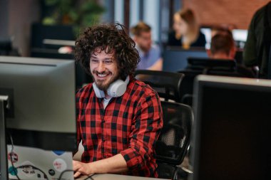 Afro saç stili ve ekose gömlekli bir programcı, modern ofis ortamındaki bir bilgisayarda özenle kodluyor.
