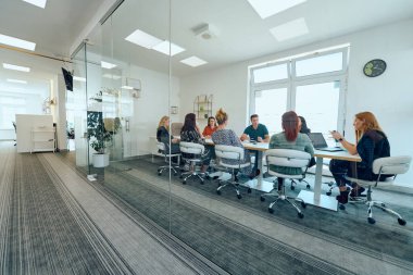 Çeşitli iş adamları modern cam duvarlı bir ofisteki projeler hakkında tartışmaya giriştiler.. 