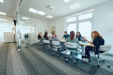 Çeşitli iş adamları modern cam duvarlı bir ofisteki projeler hakkında tartışmaya giriştiler.. 