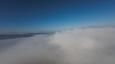 Dağlarda taze bir sabahta inanılmaz güzel bir bulutun içinden uçmak. Beyaz tüylü bulutlardan oluşan FPV insansız hava aracı açık mavi gökyüzünde usulca hareket ediyor