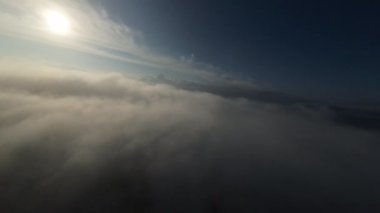 Dağlarda taze bir sabahta inanılmaz güzel bir bulutun içinden uçmak. Beyaz tüylü bulutlardan oluşan FPV insansız hava aracı açık mavi gökyüzünde usulca hareket ediyor