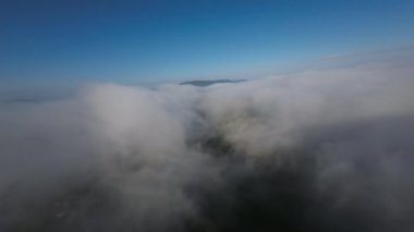 Dağlarda taze bir sabahta inanılmaz güzel bir bulutun içinden uçmak. Beyaz tüylü bulutlardan oluşan FPV insansız hava aracı açık mavi gökyüzünde usulca hareket ediyor