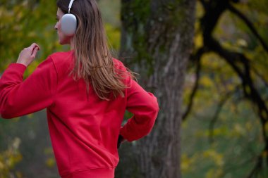 Sağlıklı yaşam tarzı, sabah koşusu. Genç ve güzel bir kadın sonbahar parkında koşuyor ve akıllı telefonuyla kulaklıkla müzik dinliyor. Kırmızı bir spor gömlek giyiyor.. 