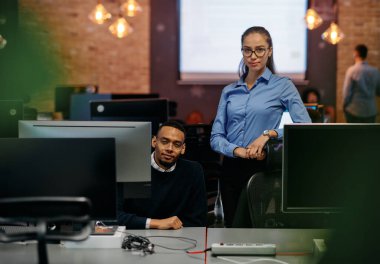 Çağdaş bir ofis ortamında, sarışın bir iş kadını ve onun Afrikalı Amerikalı iş ortağı, internetteki belgelere odaklanmış bir kararlılıkla bakıyorlar.