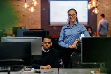 Çağdaş bir ofis ortamında, sarışın bir iş kadını ve onun Afrikalı Amerikalı iş ortağı, internetteki belgelere odaklanmış bir kararlılıkla bakıyorlar.