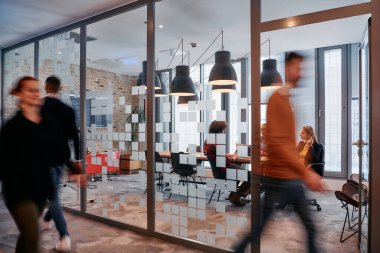 İş ortamının hareketli koşuşturmasında, bir grup genç iş adamı ofislerinin yanındaki koridorda yürürken, meslektaşları içeride iş birliği yaparak,