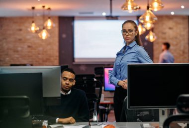 Çağdaş bir ofis ortamında, sarışın bir iş kadını ve onun Afrikalı Amerikalı iş ortağı, internetteki belgelere odaklanmış bir kararlılıkla bakıyorlar.