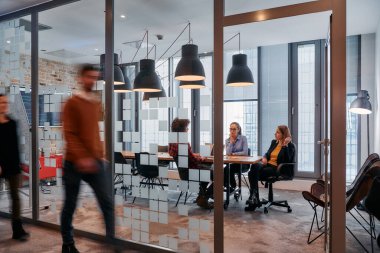 İş ortamının hareketli koşuşturmasında, bir grup genç iş adamı ofislerinin yanındaki koridorda yürürken, meslektaşları içeride iş birliği yaparak,