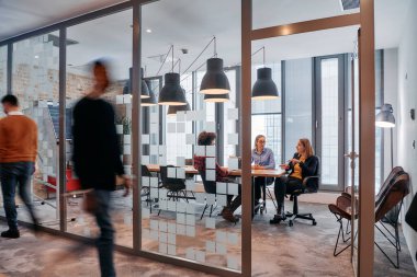 İş ortamının hareketli koşuşturmasında, bir grup genç iş adamı ofislerinin yanındaki koridorda yürürken, meslektaşları içeride iş birliği yaparak,