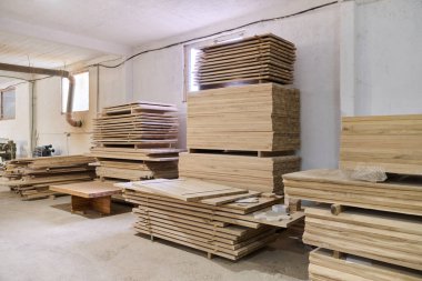 Çeşitli ahşap parçalar ve tahtalar CNC ahşap makinelerinde daha fazla işlem için hazırlanan bir depoda düzenli olarak depolanır..