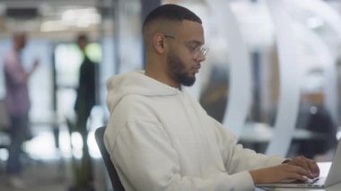 Modern ofis ortamında, Afrikalı Amerikalı bir işadamı özenle dizüstü bilgisayarı üzerinde çalışıyor, profesyonel çevresindeki kararlılığı, hırsı ve verimliliği somutlaştırıyor.. 