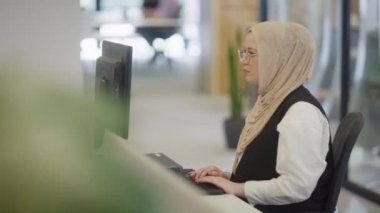 Modern bir ofiste, başörtüsü takan Müslüman bir girişimci güvenli ve gayretli bir şekilde bilgisayarında oturur, kararlılığı, yaratıcılığı ve iş dünyasının güçlendirilmesini somutlaştırır.. 