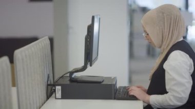 Modern bir ofiste, başörtüsü takan Müslüman bir girişimci güvenli ve gayretli bir şekilde bilgisayarında oturur, kararlılığı, yaratıcılığı ve iş dünyasının güçlendirilmesini somutlaştırır.. 