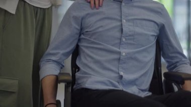 Genç iş arkadaşları, işbirlikçi iş arkadaşları, aralarında tekerlekli sandalyedeki bir kişinin de bulunduğu, modern cam ofis koridorunun yanından geçerek, çeşitliliği, takım çalışmasını ve güçlendirmeyi resmediyorlar.