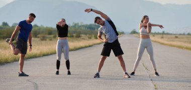 Kararlı bir grup sporcu koşularından önce kolektif bir esneme oturumuna katılıyor, takım çalışmasını teşvik ediyor ve fitness hedeflerini gerçekleştirmek için hazırlık yapıyorlar..