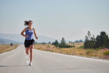 An athletic woman finds freedom and joy in a healthy lifestyle, running through a beautiful road trail at sunrise.  clipart