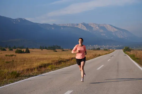 stock image A resolute and motivated athlete running confidently into the sunrise, epitomizing determination and empowerment in her early morning run. 