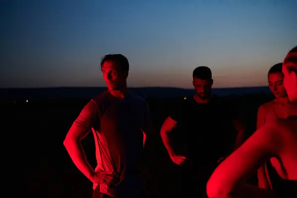 stock image In the late-night hours, a diverse group of exhausted athletes find solace under a red glow, reflecting on their day-long marathon journey and celebrating camaraderie amidst fatigue.