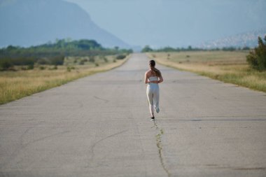 An athletic woman finds freedom and joy in a healthy lifestyle, running through a beautiful road trail at sunrise.  clipart