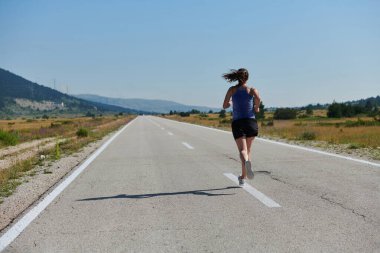 An athletic woman finds freedom and joy in a healthy lifestyle, running through a beautiful road trail at sunrise.  clipart