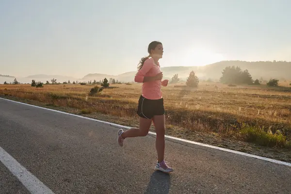 stock image A resolute and motivated athlete running confidently into the sunrise, epitomizing determination and empowerment in her early morning run. 