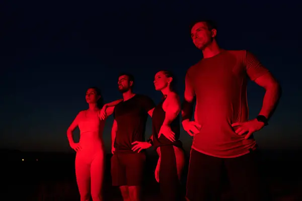 stock image In the late-night hours, a diverse group of exhausted athletes find solace under a red glow, reflecting on their day-long marathon journey and celebrating camaraderie amidst fatigue.