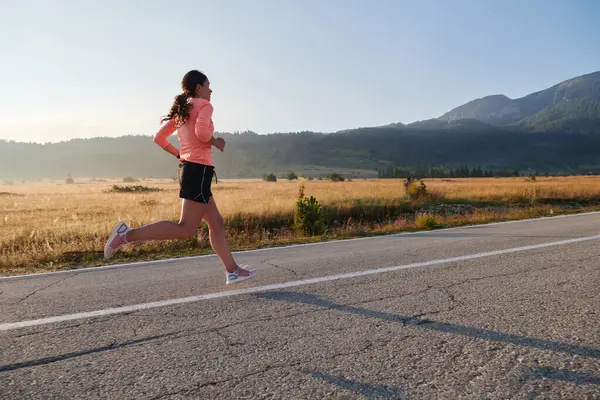 stock image A resolute and motivated athlete running confidently into the sunrise, epitomizing determination and empowerment in her early morning run. 