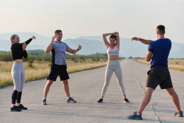 Kararlı bir grup sporcu koşularından önce kolektif bir esneme oturumuna katılıyor, takım çalışmasını teşvik ediyor ve fitness hedeflerini gerçekleştirmek için hazırlık yapıyorlar..