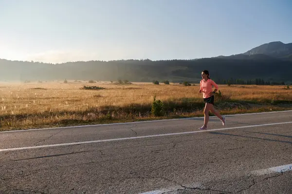 stock image A resolute and motivated athlete running confidently into the sunrise, epitomizing determination and empowerment in her early morning run. 