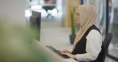 Modern bir ofiste, başörtüsü takan Müslüman bir girişimci güvenli ve gayretli bir şekilde bilgisayarında oturur, kararlılığı, yaratıcılığı ve iş dünyasının güçlendirilmesini somutlaştırır.. 