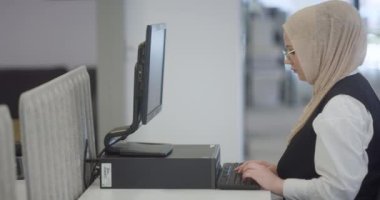 Modern bir ofiste, başörtüsü takan Müslüman bir girişimci güvenli ve gayretli bir şekilde bilgisayarında oturur, kararlılığı, yaratıcılığı ve iş dünyasının güçlendirilmesini somutlaştırır.. 