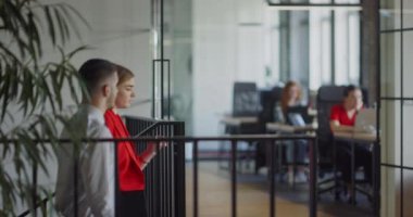 İki genç iş arkadaşı modern bir ofiste yürüyor ve çeşitli iş sorunları hakkında dinamik bir tartışmaya giriyorlar.