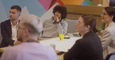 Modern cam bir ofiste çeşitli uzmanlardan oluşan bir ekip, dikkatle bir meslektaşlarını dinliyor, işbirliği ve yenilikleri teşvik ediyorlar.