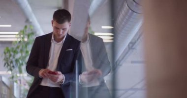  Modern bir şirket koridorunda meşgul bir işadamı, yoğun çalışma programını yönetmek ve bağlı kalmak için akıllı telefon kullanırken birden fazla iş becerisini sergiliyor. 