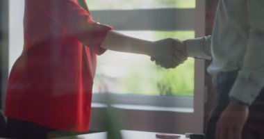 Bir yönetmen müşterisiyle olan sözleşmesini kesinleştirir, anlaşmayı sıkı bir tokalaşmayla imzalar, profesyonelliği ve modern ofis ortamındaki başarılı müşteri ilişkilerini örnek alır.