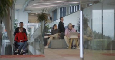 Bir şirket müdürü, iş arkadaşına tekerlekli sandalyede yardım ederek, farklı meslekdaşlarından oluşan ekiple birlikte çalıştıkları başlangıç ofislerine kadar rehberlik eder.