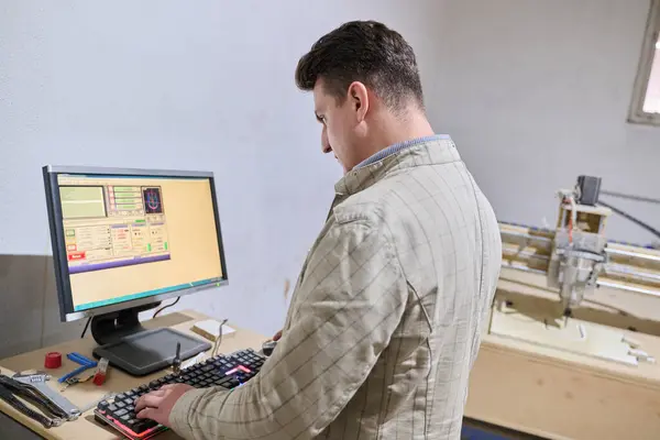 stock image Operator inputs coordinates on a computer for a CNC machine, which then precisely cuts and processes wooden pieces.