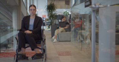 Modern bir şirkette iş arkadaşlarıyla birlikte tekerlekli sandalyedeki bir iş kadını, iş yerinin kapsayıcılığa, çeşitliliğe ve işbirliğine değer verdiğini sembolize ediyor..