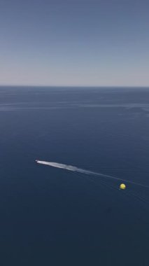 Bir tekneye bağlı paraşütle uçmanın havadan izlenen su sporları eğlencesi. Ekstrem yaz sporları plaj turizmi. Yüksek kalite 4k dikey görüntü. 