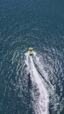 Yüksek hızda derin mavi denizde virajlar yaparken sarı sürat teknesinin yüzüşünü ve eğlenişini gösteren hava aracı görüntüsü. Yüksek kalite 4k dikey görüntü
