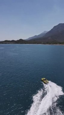 Yüksek hızda derin mavi denizde virajlar yaparken sarı sürat teknesinin yüzüşünü ve eğlenişini gösteren hava aracı görüntüsü. Yüksek kalite 4k dikey görüntü