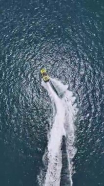 Yüksek hızda derin mavi denizde virajlar yaparken sarı sürat teknesinin yüzüşünü ve eğlenişini gösteren hava aracı görüntüsü. Yüksek kalite 4k dikey görüntü