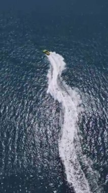 Yüksek hızda derin mavi denizde virajlar yaparken sarı sürat teknesinin yüzüşünü ve eğlenişini gösteren hava aracı görüntüsü. Yüksek kalite 4k dikey görüntü