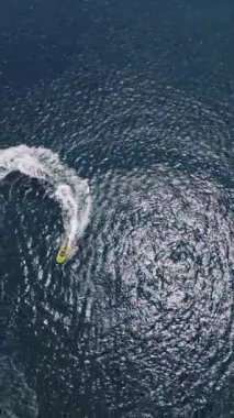 Yüksek hızda derin mavi denizde virajlar yaparken sarı sürat teknesinin yüzüşünü ve eğlenişini gösteren hava aracı görüntüsü. Yüksek kalite 4k dikey görüntü